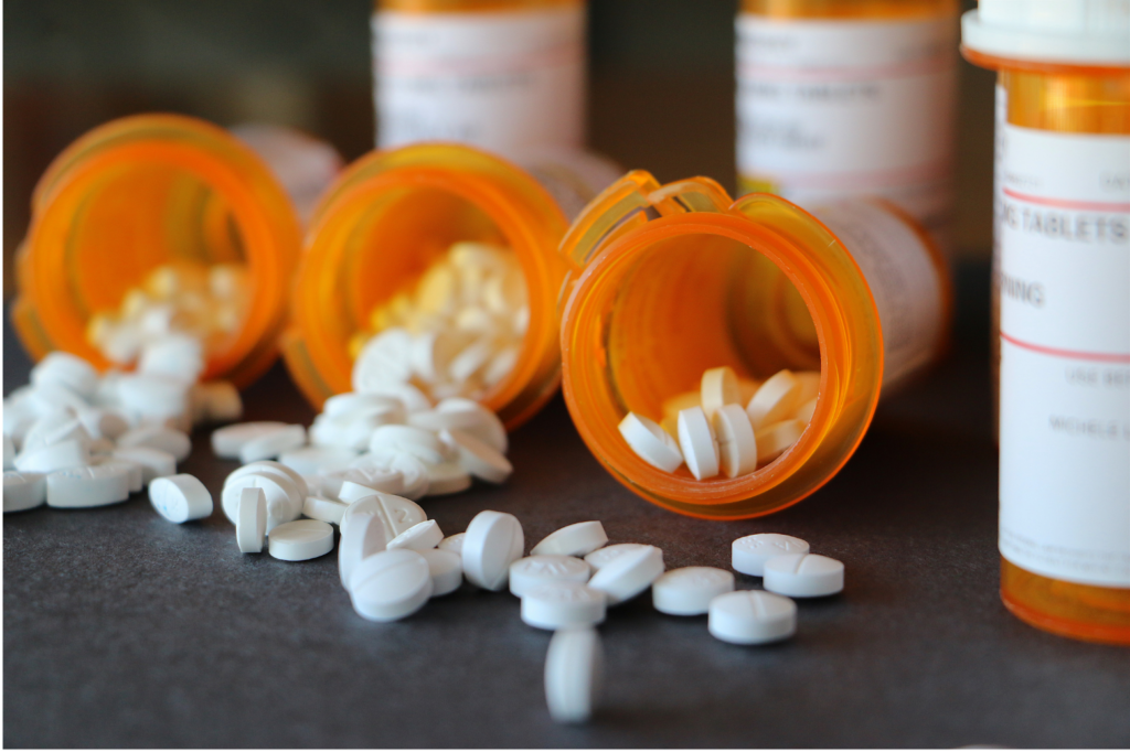 The Pill Club WARN class action. View of three prescription bottles side by side with pills spilling out. More prescriptions in the background.
