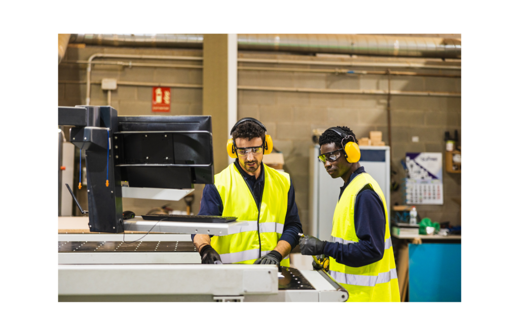 Two employees in yellow vests and wearing hearing protections are standing at an advanced printing machine.