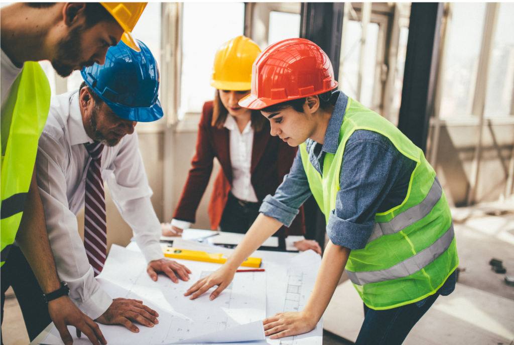 Katerra WARN class action settlement. Several male and female constructions workers reviewing blueprints in a partially finished building.