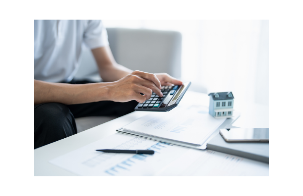 Live Well Financial WARN class action. View of person using a calculator to add up numbers for a potential mortgage. Financial forms and a small house shown slightly blurry in the background.