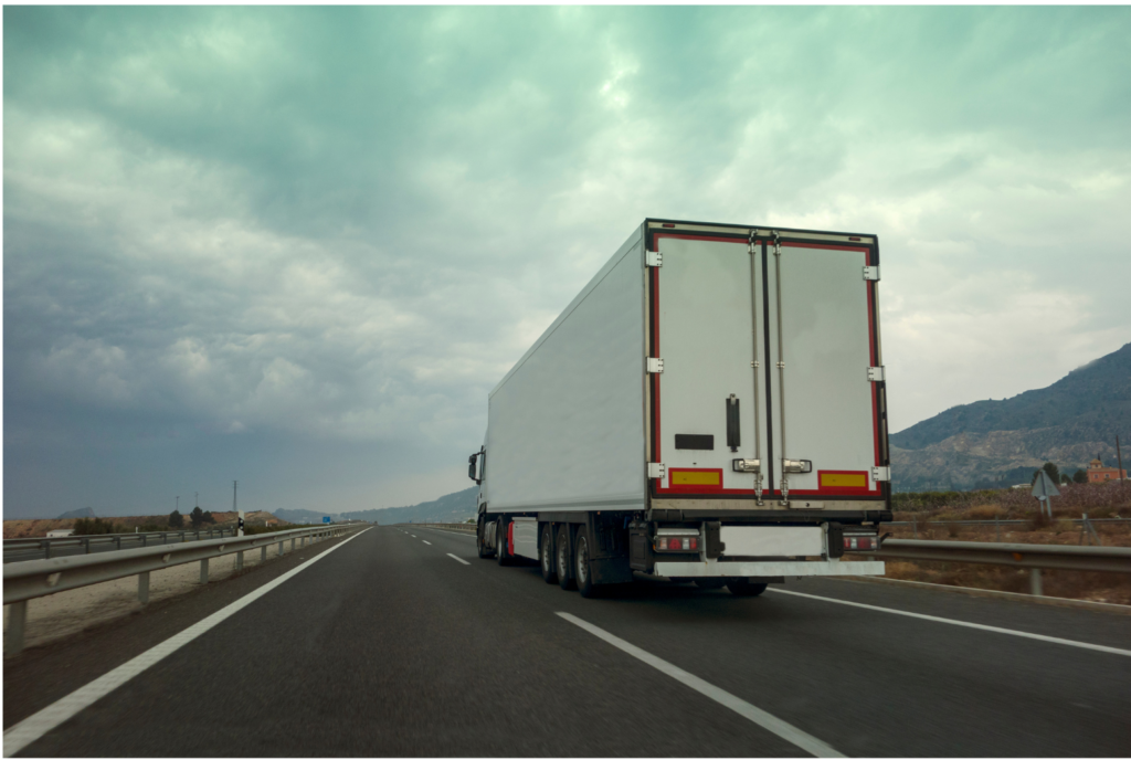 Yellow Trucking WARN class action. View of a white tractor trailer heading away from the camera on a two lane rural highway. Mountains shown in the background.