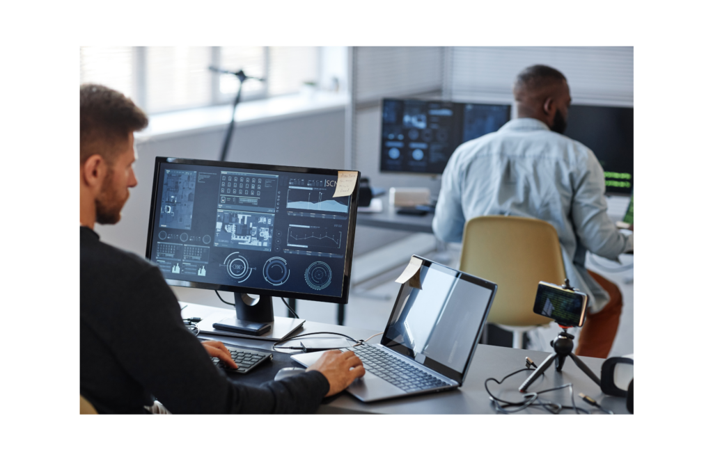 GDIT WARN class action. View of two software developers, both using multiple computer screens, in a large modern office with bright sunlight and white walls.