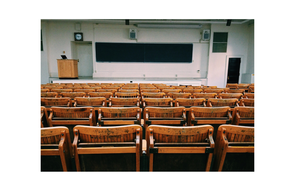 Heritage College WARN case. View of an empty college lecture hall, with folded up wooden chairs, a podium, and wide chalkboard on the back wall.