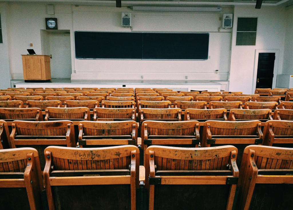 Heritage College WARN case. View of an empty college lecture hall, with folded up wooden chairs, a podium, and wide chalkboard on the back wall.