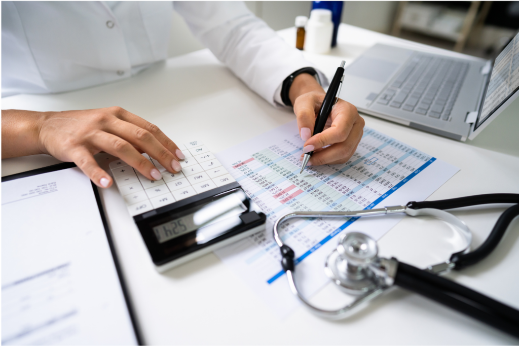 Xtend Healthcare WARN case. View of a person's hands holding a pen and using a calculator. Below the hands are medical billing charts. To the left is a laptop and three pill bottles. In the foreground, a stethoscope lies on the desk.