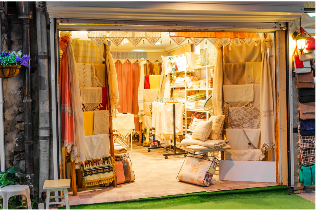 Anna's Linens WARN class action. View of a linen store with numerous items made of fabric on display, along with a number of satchels. There are dresses, sheets, table cloths, etc. of numerous colors--mostly white and pastels.