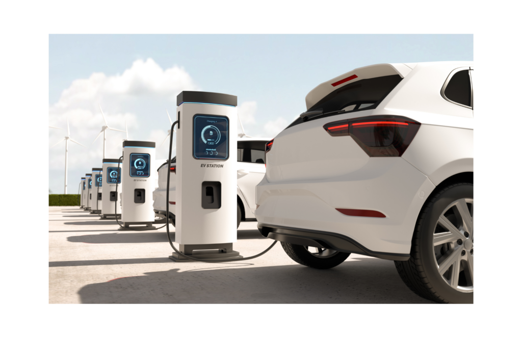 Canoo WARN class action. View of two new, white, electric vehicles at EV charging stations. In the background are numerous other charging stations and massive wind turbines in the distance.
