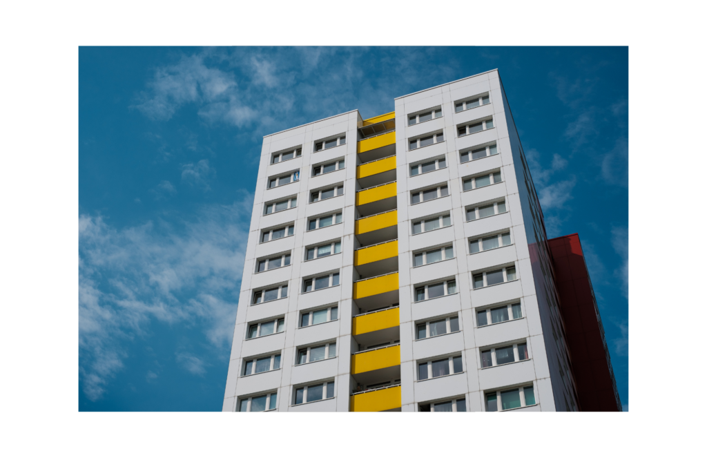 Crowne Architectural WARN class action. View of a white multi-story (at least 10) building. The building is white on the left and right, with each side showing two wide windows. Dividing the two sides of the building are walkways painted in yellow.