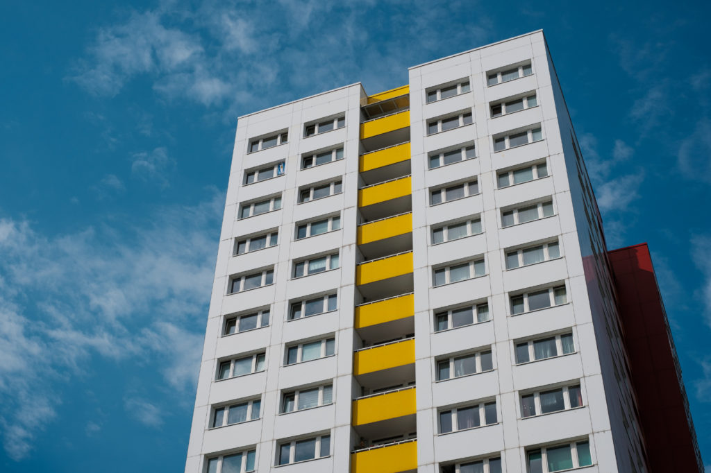 Crowne Architectural WARN class action. View of a white multi-story (at least 10) building. The building is white on the left and right, with each side showing two wide windows. Dividing the two sides of the building are walkways painted in yellow.