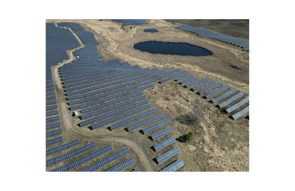 DC Solar WARN class action. View of a large solar field with the solar panels looking somewhat like a jigsaw puzzle. The panels are built in a dry field with scrubby vegetation. There are a couple of small ponds amidst the solar field of panels.