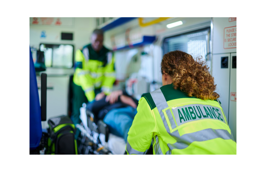 FirstMed EMS WARN class action. View of two ambulance workers wearing neon green/yellow jackets with forest green and gray reflective markings putting a patient into an ambulance on a gurney. The first responder closest to the camera is in focus. Otherwise everything else is blurry.