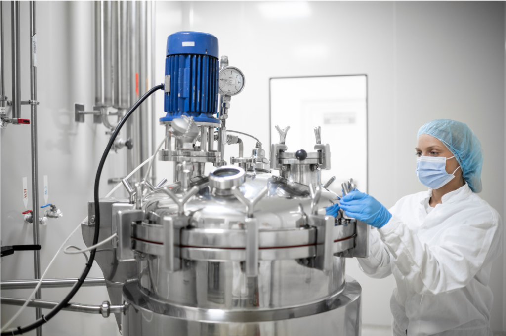 Pear Therapeutics WARN class action. View of a technician in a white jumpsuit wearing gloves, a mask, and a hairnet checking the knobs on a large medical compressor of some sort. The rooms seems almost sterile with white walls and pipes for hot and cold water extending from one wall.