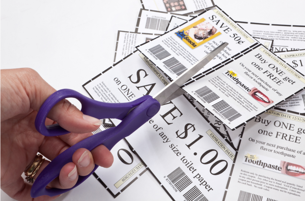 Pennysaver WARN class action. View of a women's left hand using purple handled scissors to trim coupons. There is a small pile of already trimmed coupons. The coupons are generally white with pictures. This is all shown against a white background.