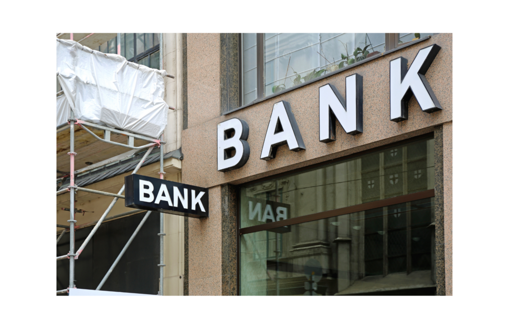 Peregrine Financial Group WARN class action. View of the first floor front face of building with word BANK presented in raised white lettering. There is also a black sign extending perpendicular from the building with the word BANK printed in white lettering. Beside the bank, an attached building has scaffolding in front of it.
