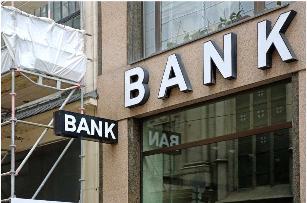 Peregrine Financial Group WARN class action. View of the first floor front face of building with word BANK presented in raised white lettering. There is also a black sign extending perpendicular from the building with the word BANK printed in white lettering. Beside the bank, an attached building has scaffolding in front of it.