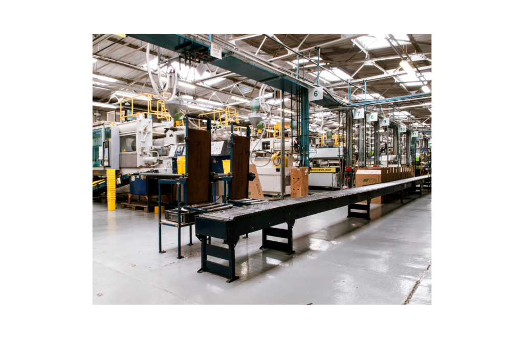 Product Quest WARN class action. Wide view of a manufacturing plant with a long conveyer belt in the middle of the room. Behind that are a series of large industrial machines connected to hoses.