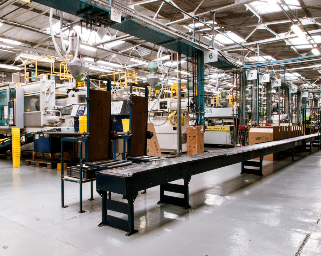 Product Quest WARN class action. Wide view of a manufacturing plant with a long conveyer belt in the middle of the room. Behind that are a series of large industrial machines connected to hoses.