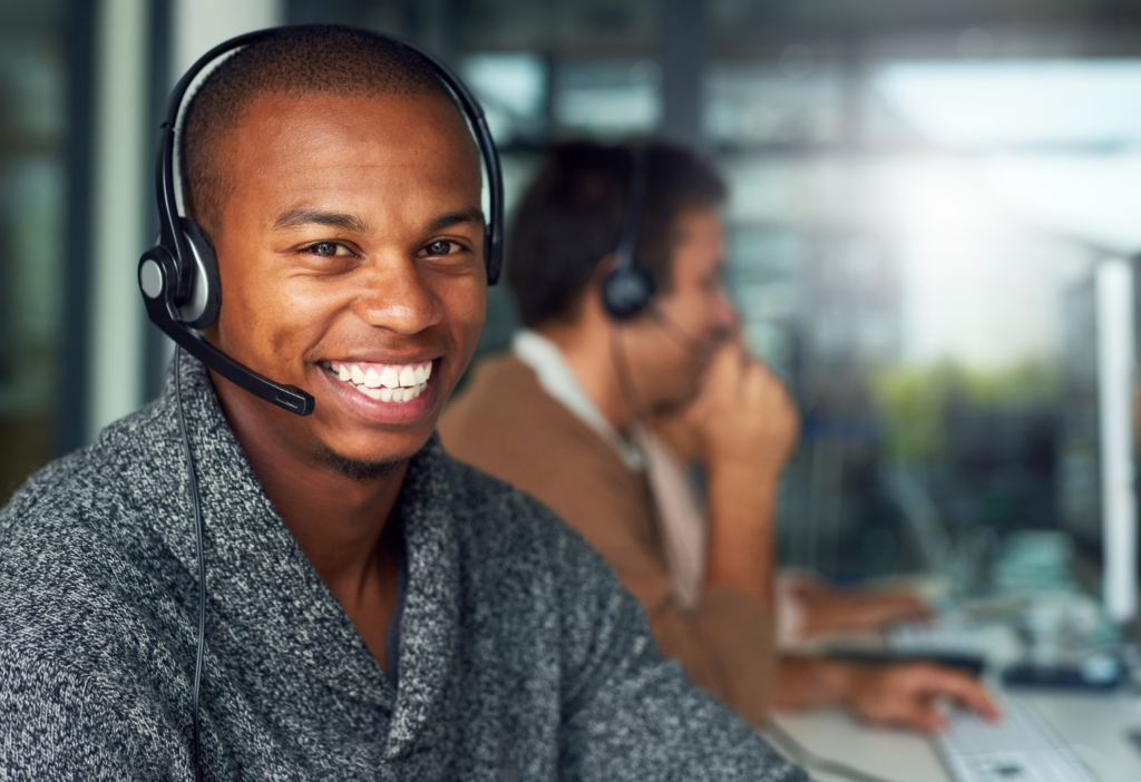 Results CSX WARN class action. Close up view of person in a telephone headset smiling at the camera. A co-worker in the call center is in the background.