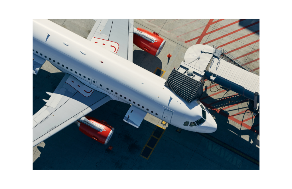 Overhead view of a large multi-engine commercial airliner at the gate of a modern airport. The walkway for passengers is extended to meet the aircraft.