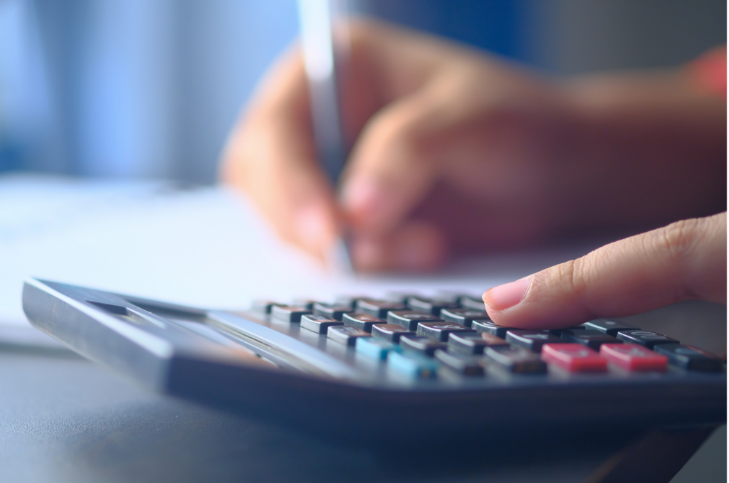 Strategic Financial WARN class action. Close up view, left hand on a calculator, blurry in the background is a hand holding a pen.