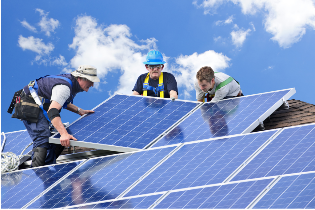 Sungevity WARN class action. View of a crew of three men in construction gear--tool belts held up with large colorful suspenders (one in blue suspenders, one green, and one yellow) installing solar panels on a shingled roof. One worker is wearing a blue hard hat.