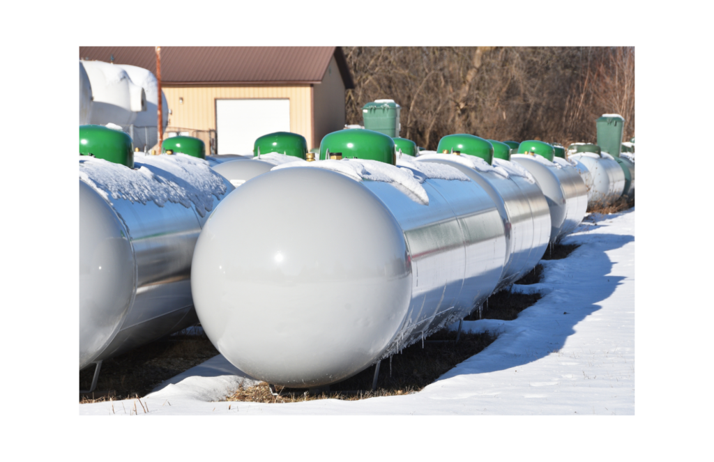 Worley & Obetz | Amerigreen Propane WARN class action. View of rows of gray large propane tanks with green caps. Each tank appears to be 8-10 feet wide and four feet high. There is snow on the ground and the tops of the propane tanks. Buildings and trees are shows in the background.