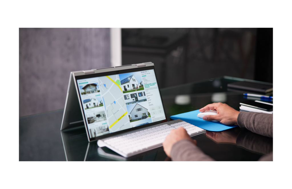 Xceligent WARN class action. View of a man reviewing real estate listings on a large table with an external keyboard on a large black desk or table. The man is using a white mouse on a blue mousepad. Paper and pen blurred out are shown on the right of the desk.